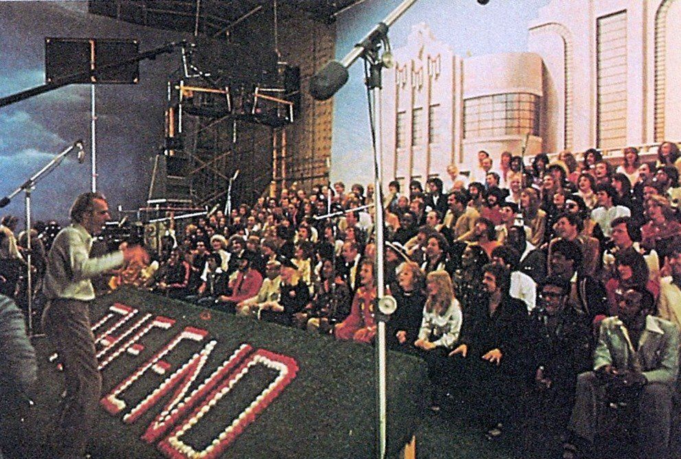 George Martin directing the cast of Sgt. Peppers lonely hearts club band movie all sitting in rows for the end of the movie